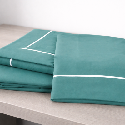 Conjunto de lençóis verdes com fita branca sobre superfície de madeira.