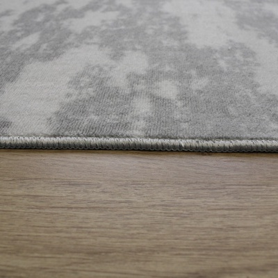 Tapete cinzento claro com padrão abstrato e bordas costuradas sobre chão de madeira