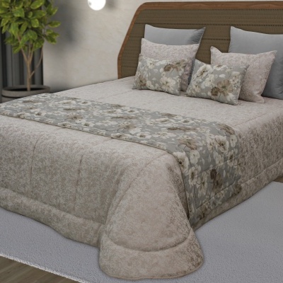 Colcha bege com padrão discreto e faixa cinzenta floral numa cama com cabeceira de vime