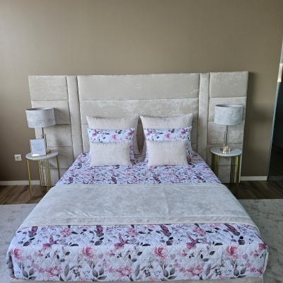 Cama estofada creme com roupa de cama floral em rosa e lilás e duas mesas de cabeceira com lâmpadas cinza