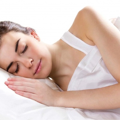 Mulher a dormir de lado com lençóis brancos e camisola branca.