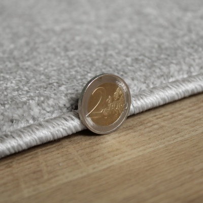 Moeda de 2 euros ao lado de tapete cinza claro sobre piso de madeira.