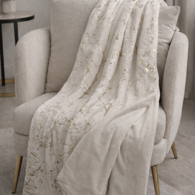 Manta creme com padrão dourado sobre poltrona creme