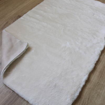 Tapete branco felpudo rectangular sobre piso de madeira clara com canto virado para cima.