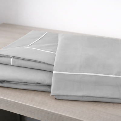 Roupa de cama cinzenta dobrada sobre superfície de madeira clara