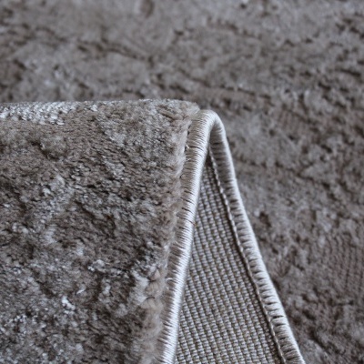 Tapete felpudo castanho claro com padrão em relevo e bordas costuradas.