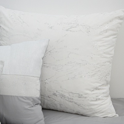 Três almofadas brancas e cinzentas com texturas diferentes sobre superfície cinzenta