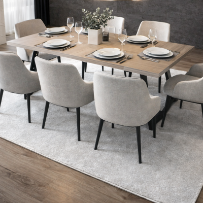 Mesa de jantar em madeira com cadeiras estofadas cinza claro e decoração de louça e plantas.