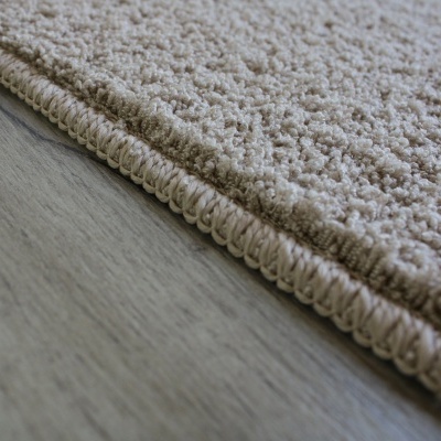 Tapete bege claro com textura de tufos grossos e bordas costuradas numa superfície de madeira clara