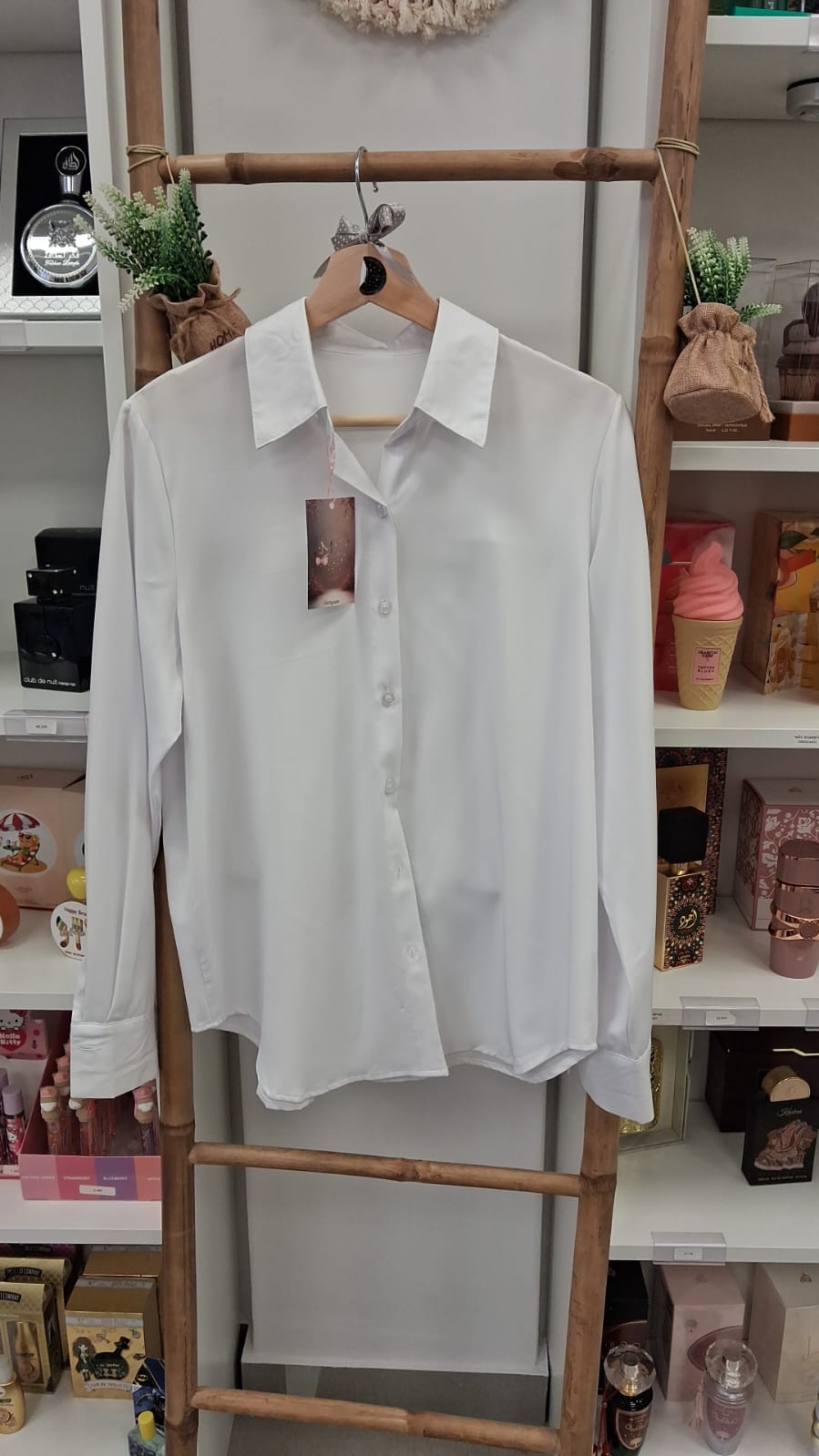 Camisa branca de manga comprida pendurada em cabide de madeira numa estrutura de bambu.