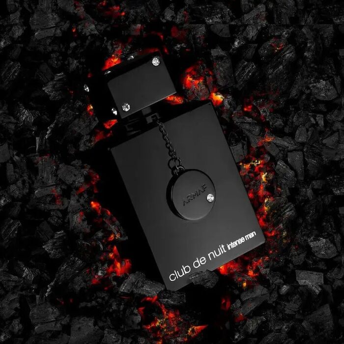 Frasco preto de perfume masculino 'club de nuit intense men' sobre carvão incandescente