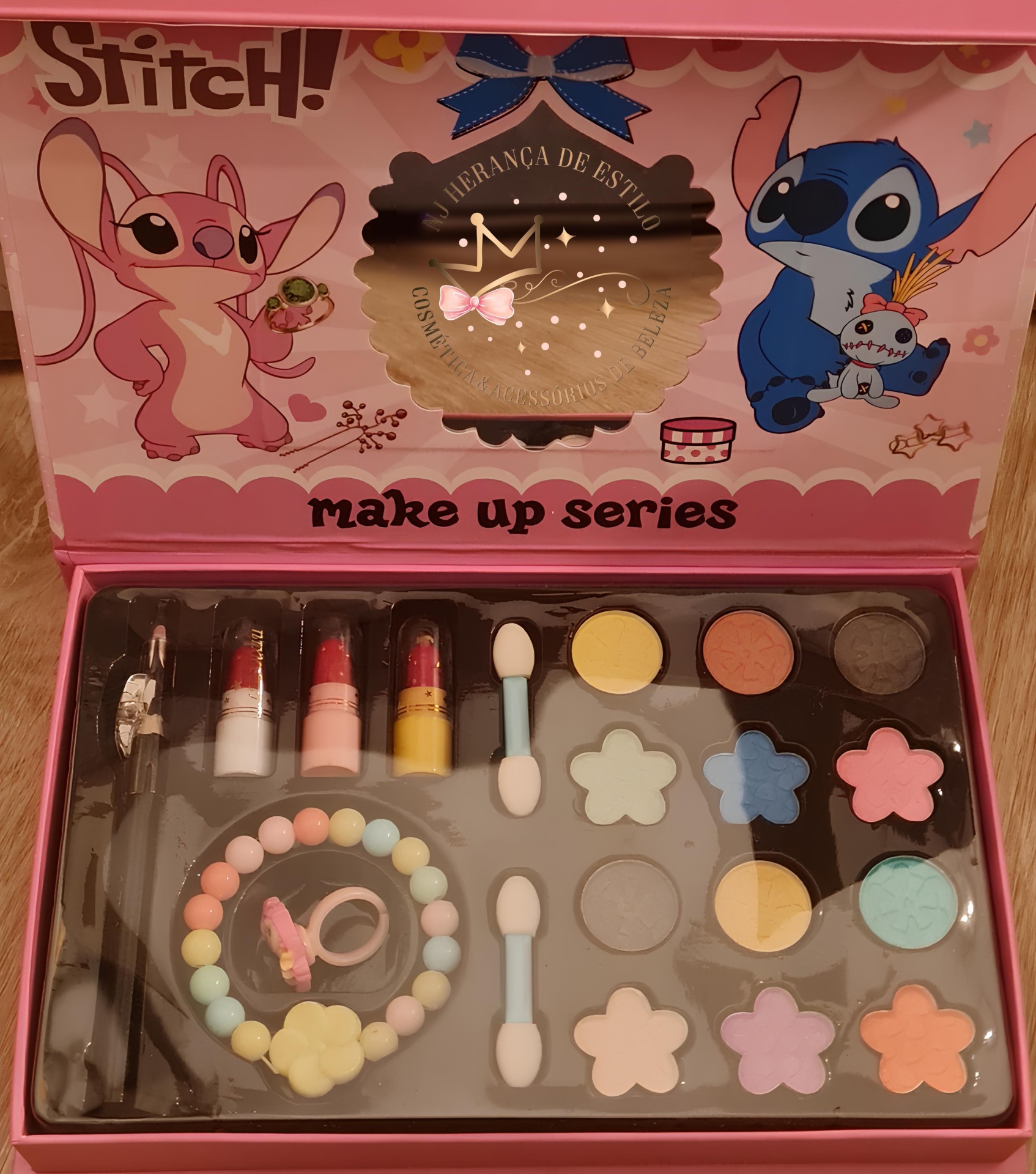 Conjunto de maquilhagem infantil com sombras coloridas, batons, acessórios e embalagem rosa com personagens Stitch