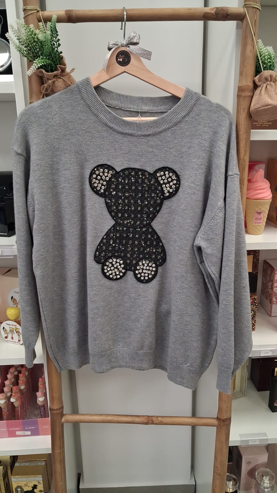 Camisola cinzenta com ursinho preto com brilhantes pendurada em cabide de madeira