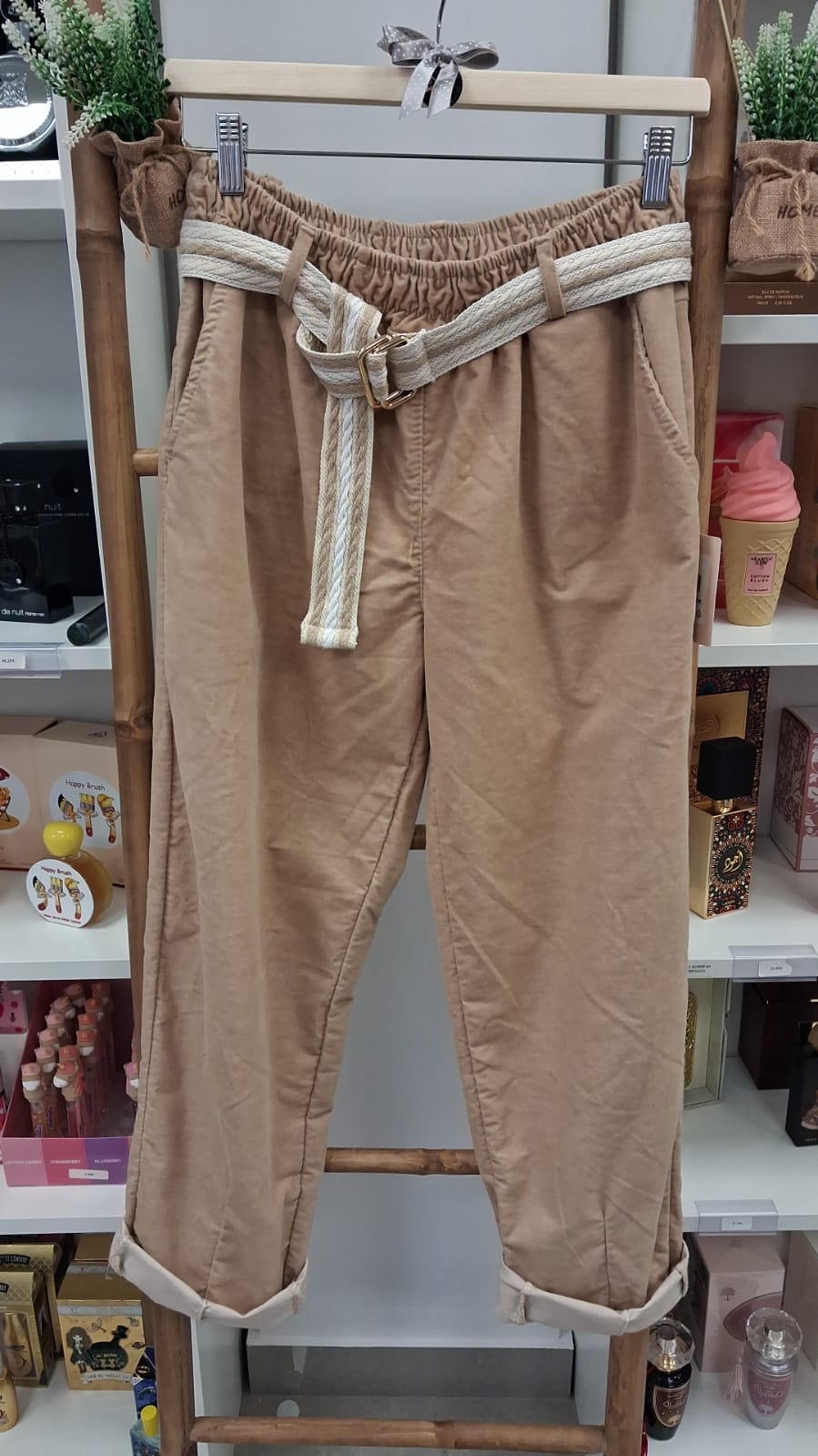 Calças bege claras com cinto branco penduradas em cabide de madeira