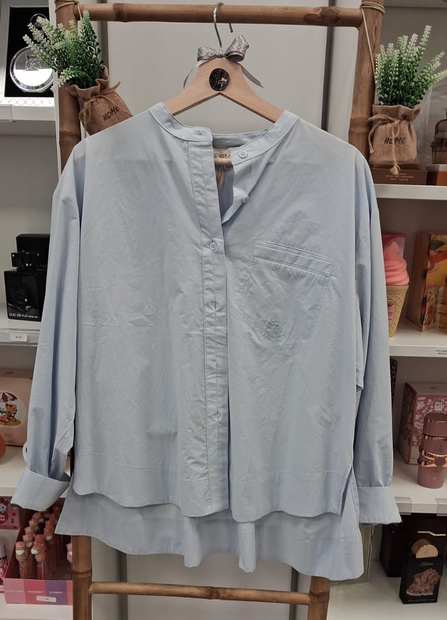Camisa azul clara com gola mandarim pendurada em cabide de madeira