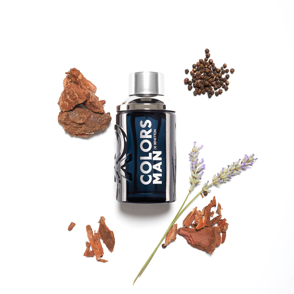 Frasco de perfume azul escuro com texto branco COLORS MAN e elementos naturais ao redor