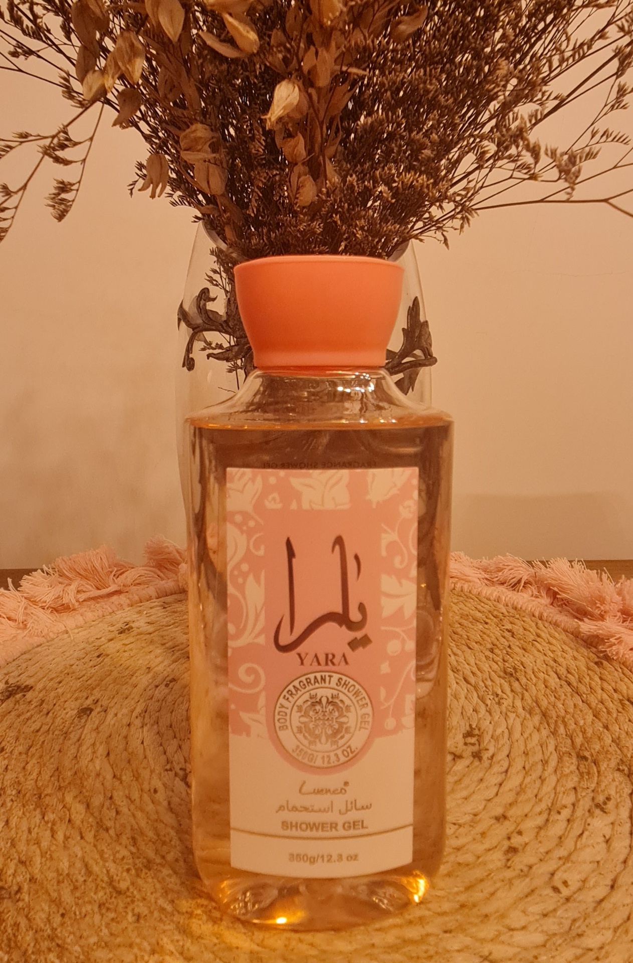 Frasco de gel de duche YARA com tampa rosa e flores secas ao fundo