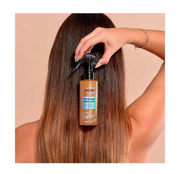 Frasco de spray para cabelo castanho com tampa negra em mão sobre cabelo castanho liso