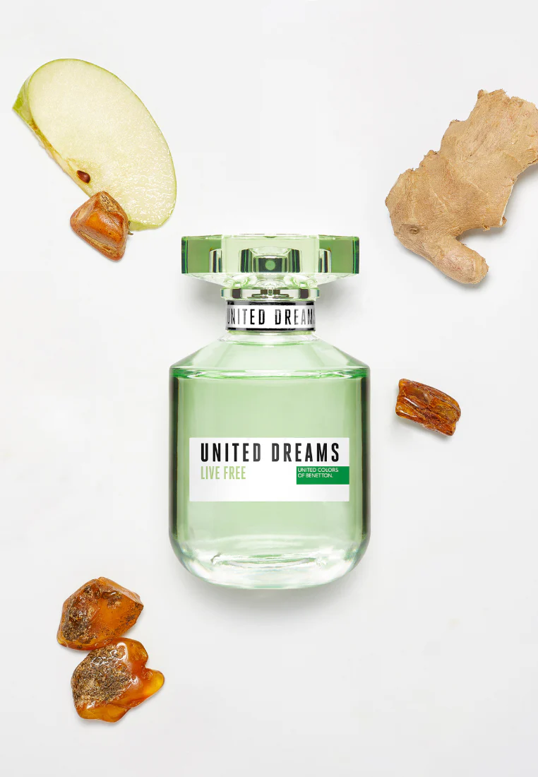 Frasco verde de perfume United Dreams Live Free com ingredientes naturais ao redor