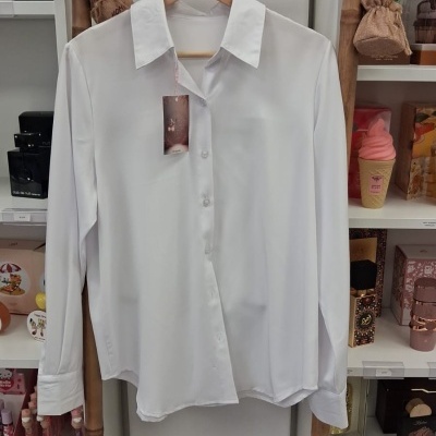 Camisa branca de manga comprida pendurada em cabide de madeira numa estrutura de bambu.