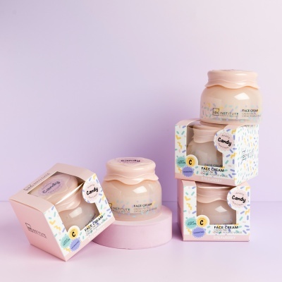 Creme facial Candy em vidro rosa claro com embalagem colorida sobre fundo rosa.