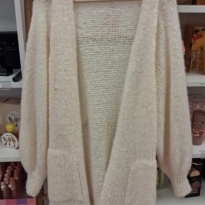 Casaco cardigan branco de malha grossa pendurado em cabide de madeira