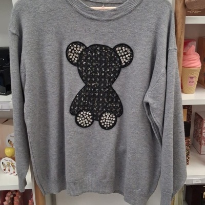 Camisola cinzenta com ursinho preto com brilhantes pendurada em cabide de madeira