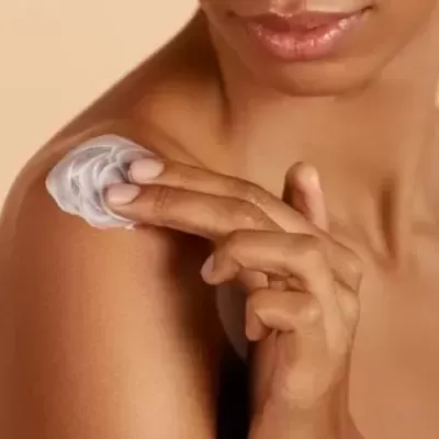Pessoa a aplicar creme branco no ombro, fundo bege