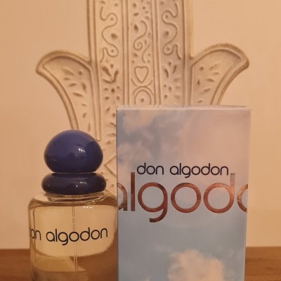 Frasco de perfume Don Algodon com embalagem azul e fundo bege com ornamento de mão