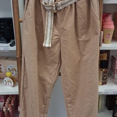 Calças bege claras com cinto branco penduradas em cabide de madeira