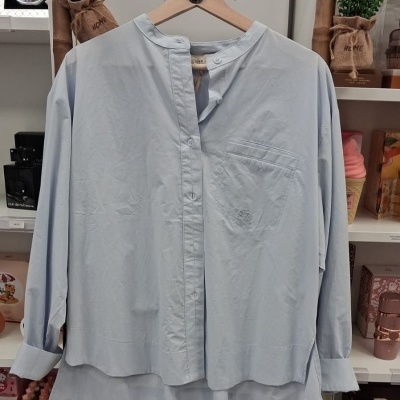 Camisa azul clara com gola mandarim pendurada em cabide de madeira