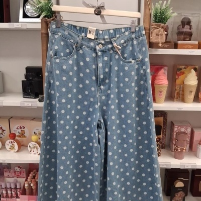 Calças largas de ganga azul com bolinhas brancas penduradas em cabide de madeira