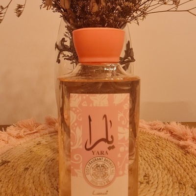 Frasco de gel de duche YARA com tampa rosa e flores secas ao fundo