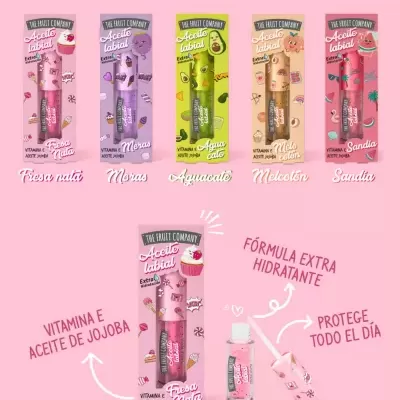 Embalagens coloridas de óleo labial The Fruit Company com texto sobre benefícios, fundo rosa.