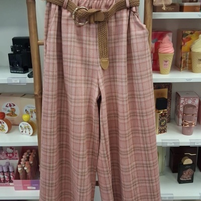Calças xadrez rosa e bege com cinto castanho penduradas num cabide de madeira