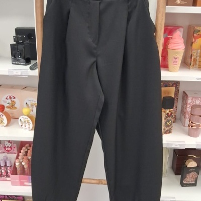 Calças pretas de tecido liso penduradas num cabide de madeira