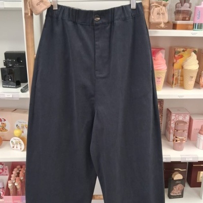 Calças pretas com cós elástico penduradas num cabide em frente a uma estante com produtos cosméticos