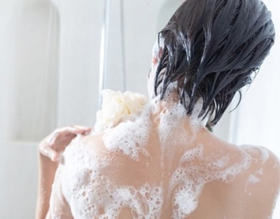 Pessoa a lavar as costas com espuma branca e esponja em banho branco