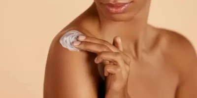 Pessoa a aplicar creme branco no ombro, fundo bege