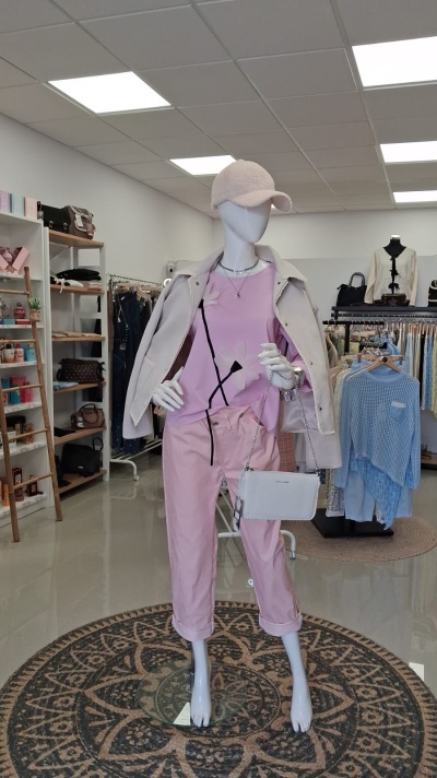 Mannequim com roupa rosa e bege, boné e mala branca em loja de roupa