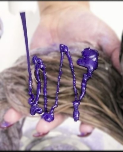 Mãos segurando cabelo com creme capilar púrpura sendo aplicado