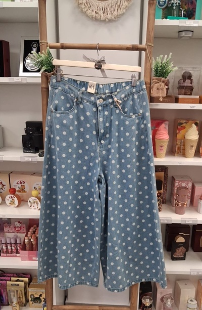 Calças largas de ganga azul com bolinhas brancas penduradas em cabide de madeira