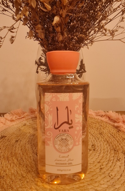 Frasco de gel de duche YARA com tampa rosa e flores secas ao fundo