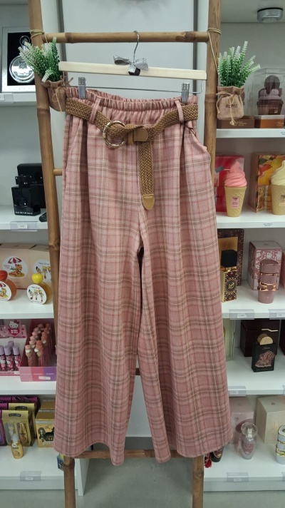 Calças xadrez rosa e bege com cinto castanho penduradas num cabide de madeira