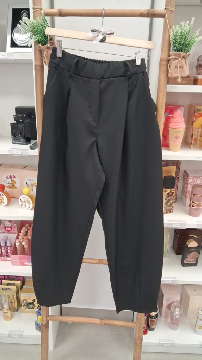 Calças pretas de tecido liso penduradas num cabide de madeira