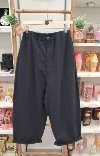 Calças pretas com cós elástico penduradas num cabide em frente a uma estante com produtos cosméticos