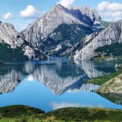 Paisagem natural com lago refletindo montanhas e colinas verdes.