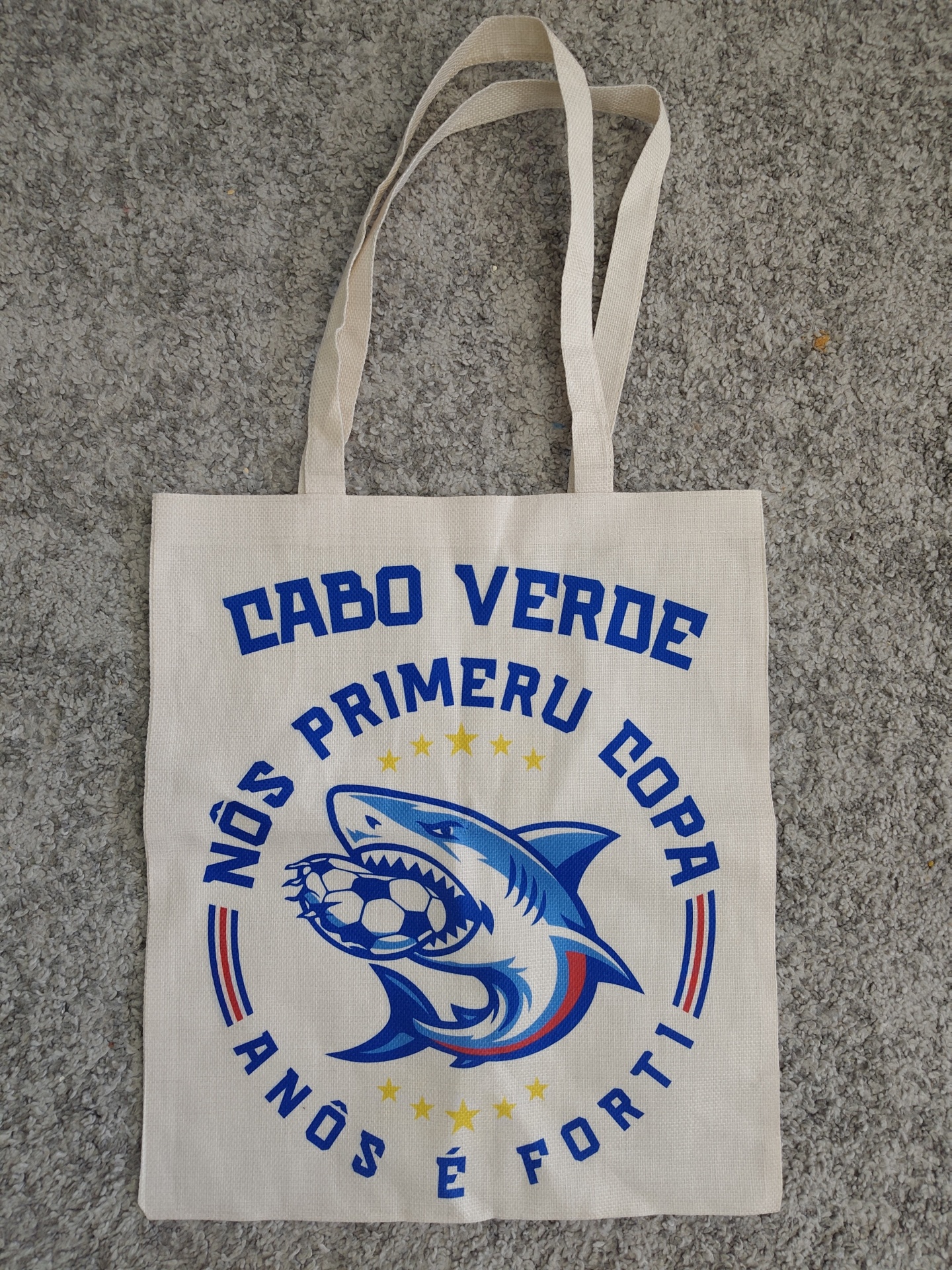 Saco de pano bege com texto azul e ilustração de tubarão com bola de futebol.