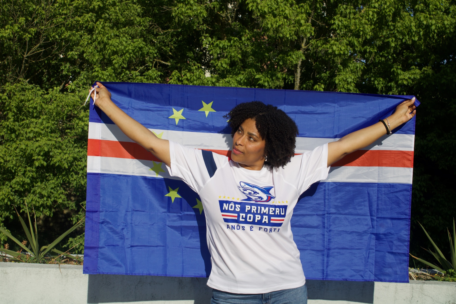 Pessoa segura bandeira azul com estrelas e riscas e veste t-shirt branca com estampado e texto