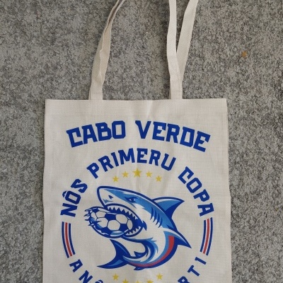 Saco de pano bege com texto azul e ilustração de tubarão com bola de futebol.